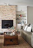 Living room with fireplace, stone wall, light grey sofa and chest as coffee table