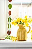 Daffodils (Narcissus) in a yellow vase on a windowsill with Easter decorations