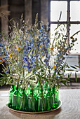 Dried meadow flowers in green glass bottles on a round tray