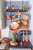 Copper pots and pans in a vintage kitchen with patterned wallpaper and candlesticks