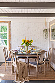 Dining room with round table, sunflowers and light-coloured wooden chairs with upholstery