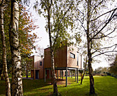 Wood-clad house on stilts with aluminium windows surrounded by trees