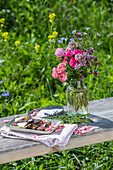 Wooden bench with bouquet of flowers and broken chocolate in the summer garden