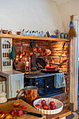 Rustikale Küche mit Kupfertöpfen vor Ziegelwand und Holzofen