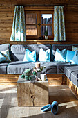 Corner sofa with grey upholstery and blue cushions in alpine wooden hut