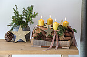 Adventsgesteck mit gelben Kerzen und Zapfen auf Holztisch