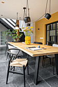 Dining area with wooden table, designer chairs and yellow accent wall in a modern design