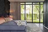 Schlafzimmer mit großem Bett, Panoramafenstern und Gartenblick