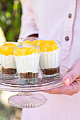 Small glasses with lemon cream and biscuit base on a cake plate with base