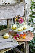 Dessert glasses and colourful flowers on cake plate with base, wooden bench outdoors