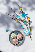 Meringues in pastel colours, branch with DIY flowers and name tag on table