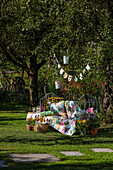 Metal bench with colourful patchwork blanket, bunting and flowers in the summer garden