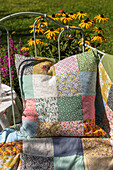 Patchwork cushion and blanket on a metal bench in the summer garden