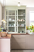 Kitchen with light grey cupboards and display cabinet, sunflowers on the worktop