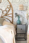 Bett mit Kopfteil aus Rattan und moderner Nachttisch mit Vase in Türkis vor floraler Tapete