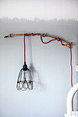 Hanging lamp with red cable attached to a driftwood frame on the wall
