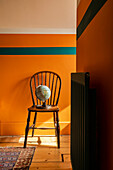 Wooden chair with globe in front of an orange-coloured wall with a turquoise stripe