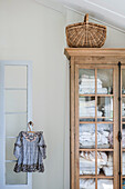 Wicker basket stands on linen cupboard, children's dress on hanger