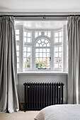 Bay window with white sash bars, black heating and grey curtains in bedroom