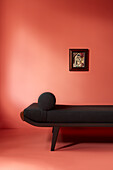 Black daybed in front of coral-coloured wall with artwork