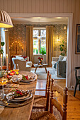 Festively laid wooden table with view into the living room with wallpaper wall