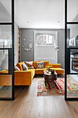 View through glass door into living room with yellow velvet sofa and oriental carpet