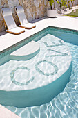 Two deckchairs next to a small pool with mosaic lettering