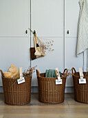 Three labelled rattan baskets for mucking out in front of a white cupboard