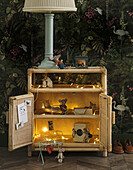 Rattan cupboard in front of jungle wallpaper with fairy lights and miniature furniture for toy mice