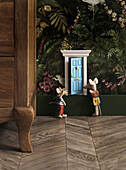 Two mouse figures in front of miniature door in floral mural