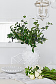 White ceramic jug with eucalyptus branches and roses on a light-coloured table