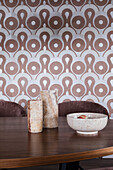 Dark wooden table with stone vases and ceramic bowl in front of retro wallpaper