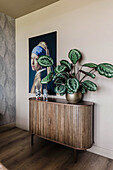 Round wooden sideboard with calathea plant and artwork on the wall