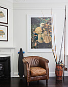 Leather armchair, longboard and jar with fishing rods in front of modern wall art