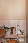 Bedroom with apricot-coloured walls, floral cushions and bedside table