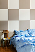 Bed with light blue bed linen in front of a chequered wall in the bedroom