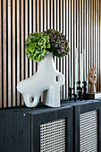 White abstract ceramic vase with hydrangeas on a dark sideboard with wickerwork, wood-panelled wall