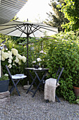 Small garden alcove with bamboo umbrella and hydrangeas, anthracite-coloured folding furniture on gravel path