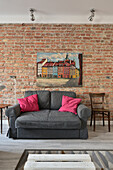 Grey sofa with pink cushions in front of brick wall and cityscape