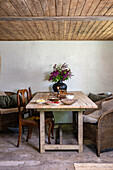 Rustic wooden table with wildflower bouquet and mixed chairs in country house flair