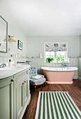 Bathroom with free-standing pink bathtub, light green interior design and striped carpet