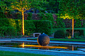 Brunnen mit beleuchteter Kugel im Garten am Abend
