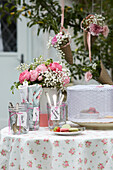 Romantic garden table with rose arrangement, cutlery in a glass, macarons and strawberries