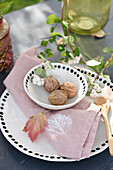 Decorative table arrangement: plate and bowl with black polka dot rim, bowl filled with walnuts, DIY cloth napkin with leaf print