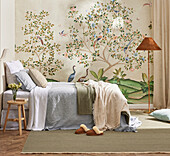 Bed with pastel-coloured bed linen in front of wallpaper with nature motif