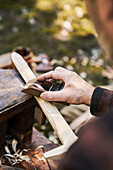 Man works on wooden sword with a plane outdoors