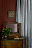 Rustic chest of drawers with mirror and floral decoration in front of a grey curtain