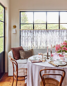 Round, laid dining table and flower arrangement in front of large window front