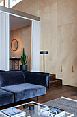 Dark blue velvet sofa in modern living room with light-coloured wooden wall