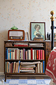 Vintage bookshelf with old radio and portrait against a patterned wallpaper background